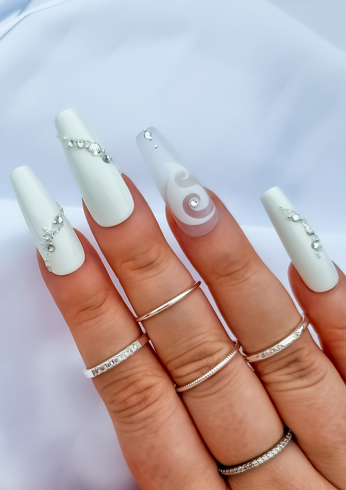 White nails with hei matau nail decal on ring finger and silver sea themed crystal design