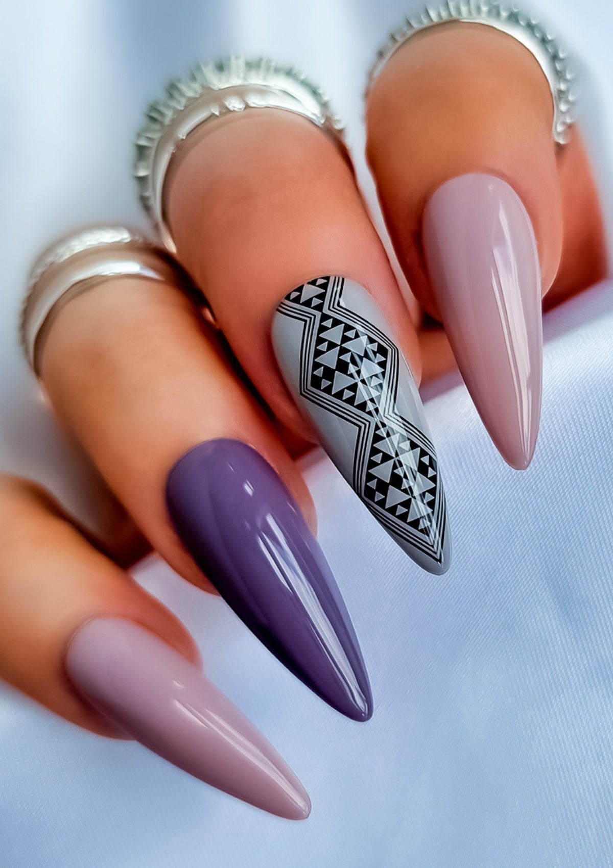 Long almond shaped nails in different shades of mauve and grey  with black Maori nail art on the middle finger. Nail art design in Aonui pattern by Adrienne Whitewood.  